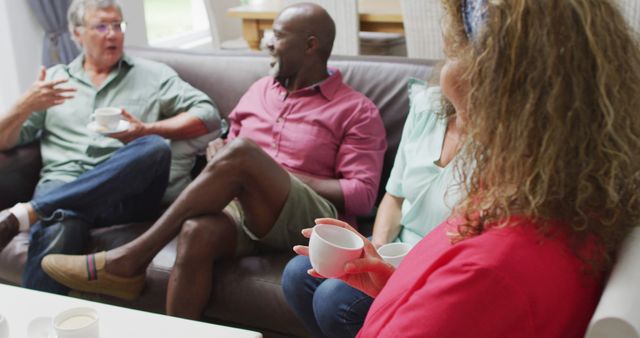 Group of multicultural friends joyfully chatting and enjoying coffee in a comfortable living room. Suitable for use in socializing, community, togetherness, and lifestyle themes.