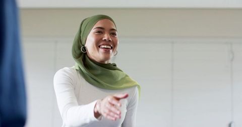 Smiling muslim businesswoman in green hijab extending hand for greeting in modern office
