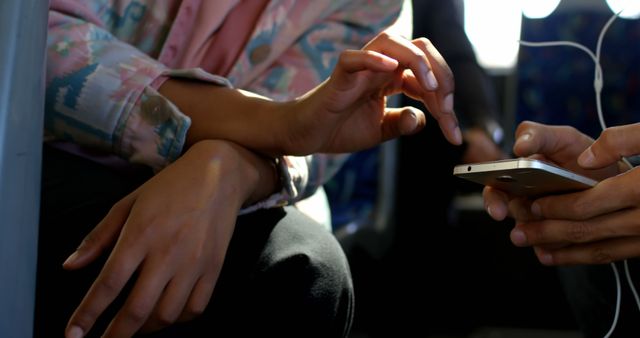 Close-up of hands using a smartphone, likely during a commute on public transportation. The passengers are engaging with the mobile device, emphasizing connectivity and interaction. Ideal for illustrating modern life, urban commuting, technology use in transit, or social interaction.