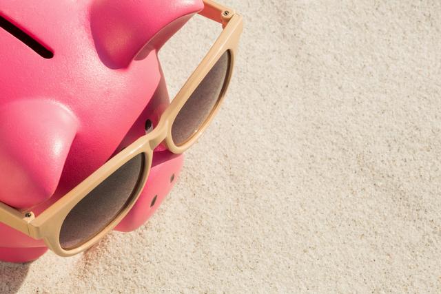 Piggy bank wearing sunglasses on sandy beach, symbolizing summer savings and financial planning. Ideal for use in articles about vacation budgeting, financial tips for holidays, or promotional materials for travel agencies.