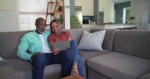 Mature african american couple relaxing on gray sectional using tablet in modern home