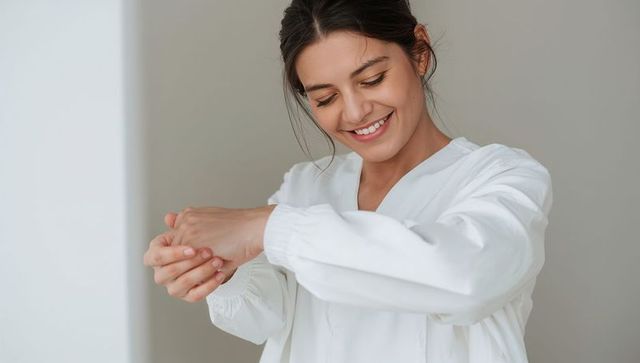 Smiling woman adjusting sleeve in minimalist interior, serene portrait, neutral decor