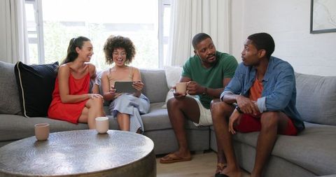 Diverse friends laughing on sofa discussing digital content