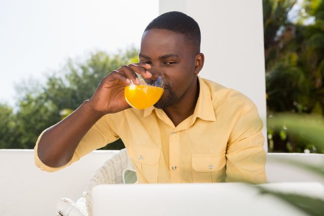 Young man drinking orange juice while looking at laptop in cafe