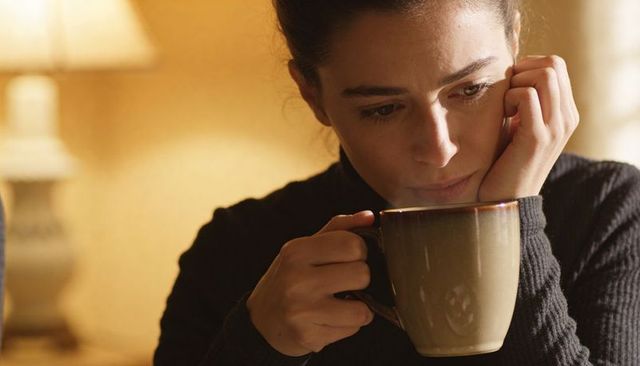 Contemplative woman cupping warm mug by lamp, cozy intimate morning reflection
