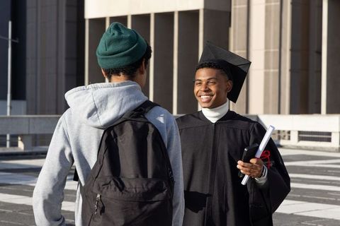 Graduating student smiling and celebrating with friend on urban campus plaza holding diploma