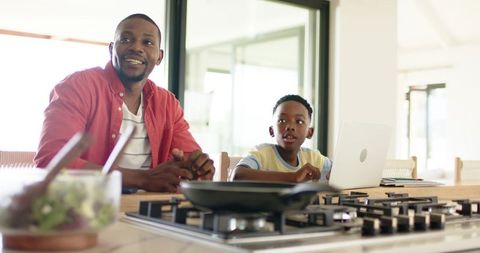 African american father and son learning online at kitchen island in bright modern home