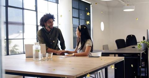 Colleagues Shaking Hands Over Documents in Modern Open-Plan Office With Natural Light