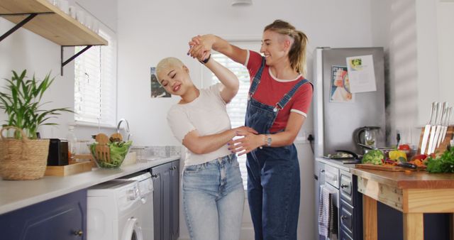 Happy diverse female couple embracing and dancing together in kitchen. spending quality time at home.
