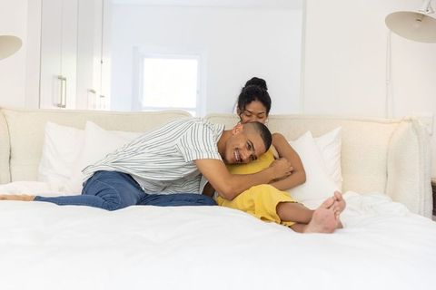 Couple cuddling on white bed in bright minimalist bedroom, cozy intimate embrace and joy