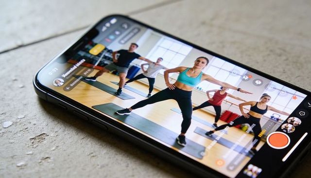 Mobile streaming fitness class with instructor leading lunges in studio on smartphone