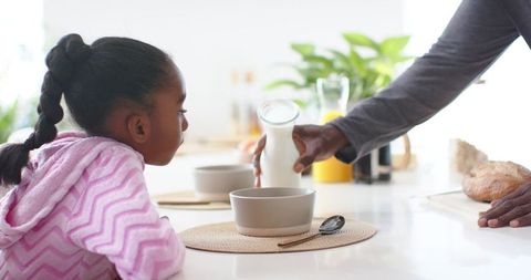 African american man pouring milk for child at morning breakfast