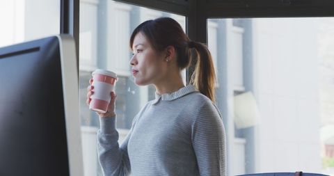 Thoughtful Businesswoman Drinking Coffee by Office Window