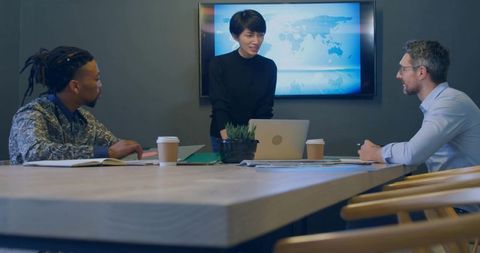 Asian woman leading boardroom presentation with world map screen, collaborative team meeting