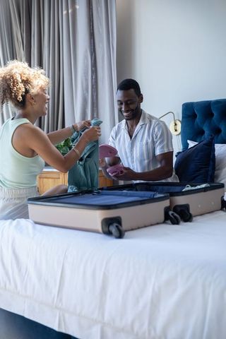 Mixed-race couple packing suitcase on bed, laughing, preparing for vacation and travel