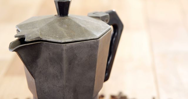 Image shows vintage metal teapot on wooden surface with scattered coffee beans. Ideal for use in websites, blogs, or publications focusing on rustic kitchen decor, traditional coffee-making utensils, or antique collections. Suitable as a background or part of an editorial piece related to coffee culture or home aesthetics.