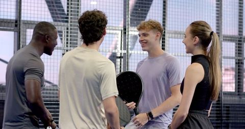 Diverse athletes chatting on padel court with fitness tracker