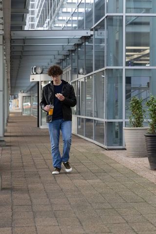 Curly-haired young man walking through glass arcade holding orange drink and snack