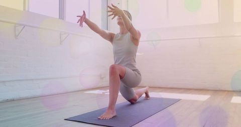 Sunlit yoga studio woman practicing low lunge stretch reaching arms for balance