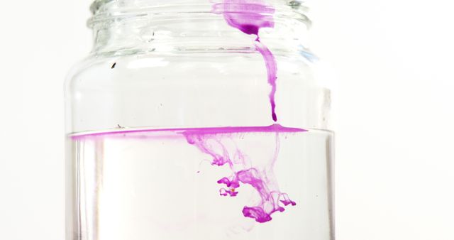 Purple ink slowly spreading in clear water inside a glass jar, highlighting fluid dynamics and diffusion process. Can be used for educational materials on liquid behavior, artistic backdrops, or creative projects emphasizing fluidity and color mixing.