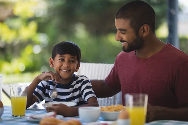 Father and son sharing a joyful breakfast outdoors, highlighting family bonding and morning routines. Ideal for use in advertisements, parenting blogs, family-oriented products, and lifestyle articles.