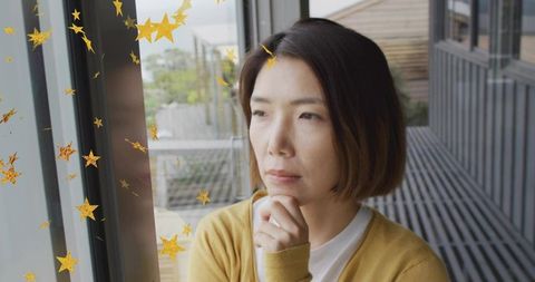 Contemplative chinese woman gazing out window resting chin on hand with gold star decals