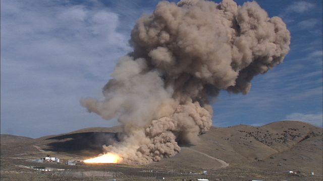 This shows a dramatic test firing of the TEM-13 solid rocket motor in support of the Ares/CLV first stage by ATK in Utah. Large smoke clouds billow into the sky from the rocket. Ideal for aerospace technology, engineering advancements, space research, and NASA-related content. Can be used in educational materials, technology reports, and aerospace engineering publications.