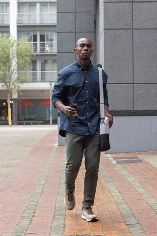 African american man walking through urban courtyard with coffee and messenger bag