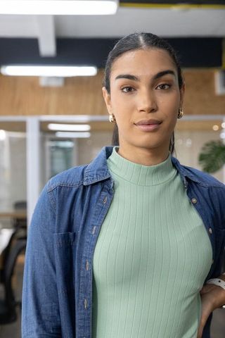 Confident female professional standing in modern coworking space wearing denim shirt