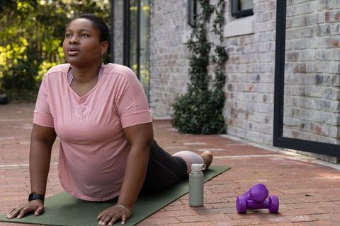 African american woman practicing cobra yoga on brick patio during outdoor home workout