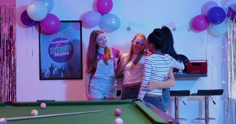 Young women celebrating at neon disco party lounge with pool table, balloons, glitter