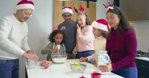 Multigenerational Diverse Family Baking Holiday Cookies at Kitchen Island Wearing Santa Hats