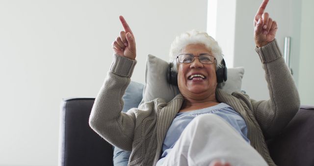 African american senior woman wearing headphones listening to music sitting on the couch at home. retirement senior lifestyle living in quarantine lockdown concept