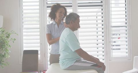 Home caregiver massaging senior man on treatment table, promoting comfort and wellness
