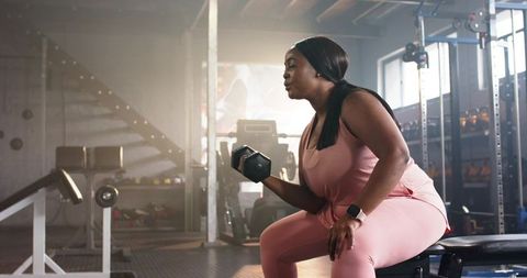 African american woman lifting dumbbell while seated on bench in gym