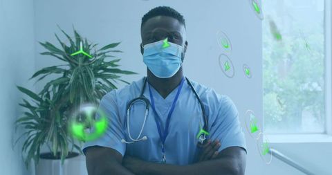 Clinician standing with crossed arms in hospital corridor wearing mask and stethoscope