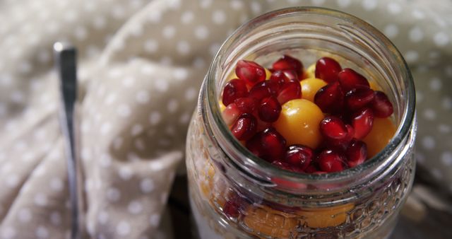 A jar filled with colorful fruit, including pomegranate seeds and a whole apricot, sits atop a polka-dotted cloth. The vibrant colors of the fruit offer a fresh and appetizing visual appeal.