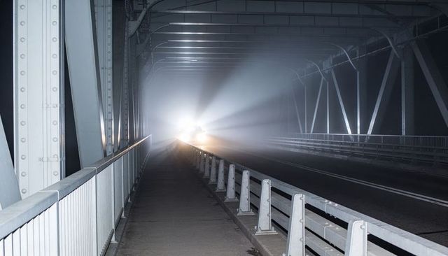 Headlights Cutting Through Fog on Steel Truss Bridge Walkway at Night