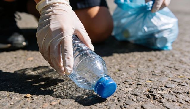 Volunteers picking up plastic bottle with gloves during community cleanup and recycling effort