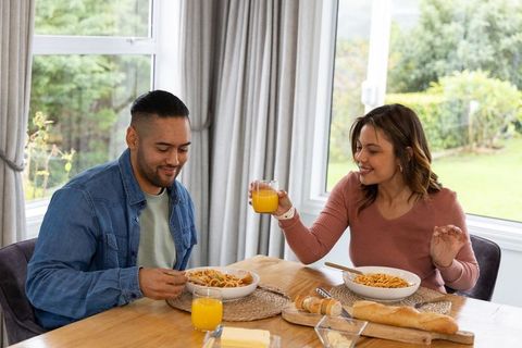 Couple sharing cozy pasta meal at home raising glass of orange juice