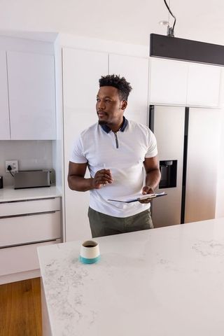 African american man checking notes at modern marble kitchen island with clipboard