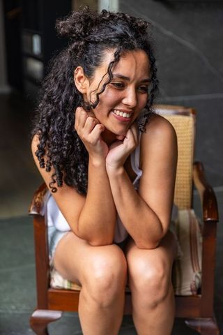 African american woman smiling and leaning forward on cane armchair, casual indoor portrait