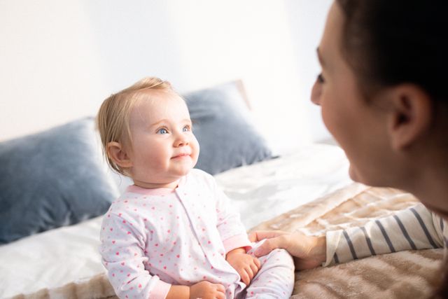 Happy caucasian mother sitting on bed talking to smiling baby daughter - Download Free Stock Photos Pikwizard.com