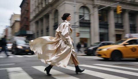 Model striding across city crosswalk wearing flowing satin trench coat in motion