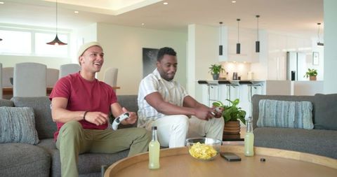 Diverse friends playing video games on sofa with snacks and drinks in modern open-plan lounge