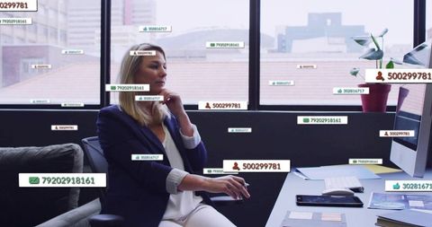Mature businesswoman resting chin while using mouse and analyzing data overlays in office