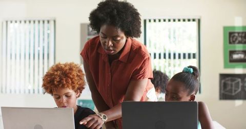African teacher guiding students on laptops in bright classroom, mentoring digital learning