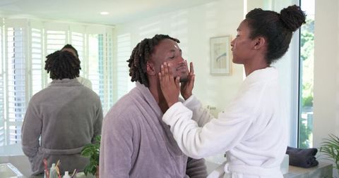 African american couple applying skincare together in sunlit bathroom mirror moment