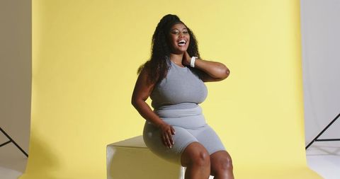 Joyful african-american woman laughing in grey activewear on yellow studio backdrop