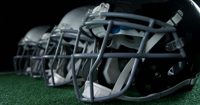Close-up of a row of football helmets on a green grass field, ideal for promoting sports equipment, athletic safety, team sports, or football events. Useful for illustrating football-related articles, advertisements, or posters.
